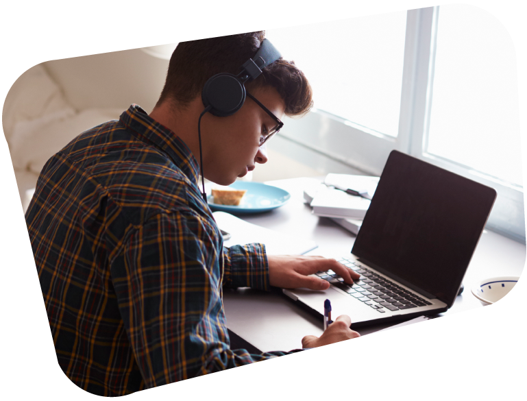 An image of a boy studying from home at a desk with his laptop, whilst wearing headphones.