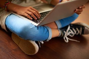 A person sat on the ground, using a laptop.