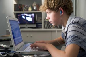 A boy using a laptop and wearing headphones. 